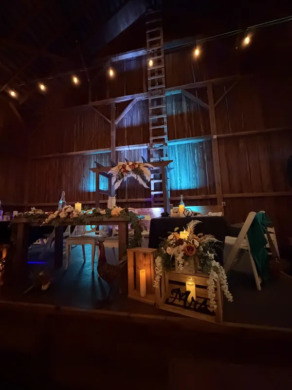 Barn reception head table lit with teal uplighting under string lights