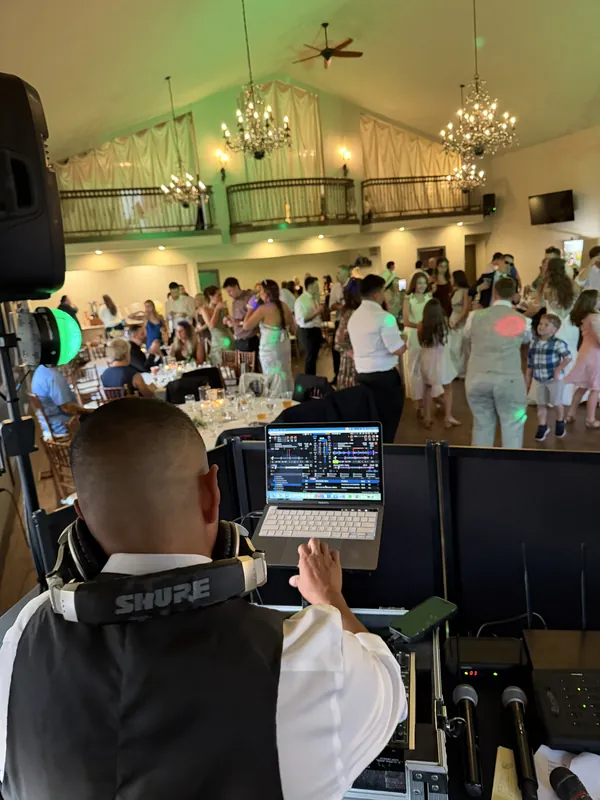 Wedding guests filling the dance floor of a chandelier hall, seen from behind the booth